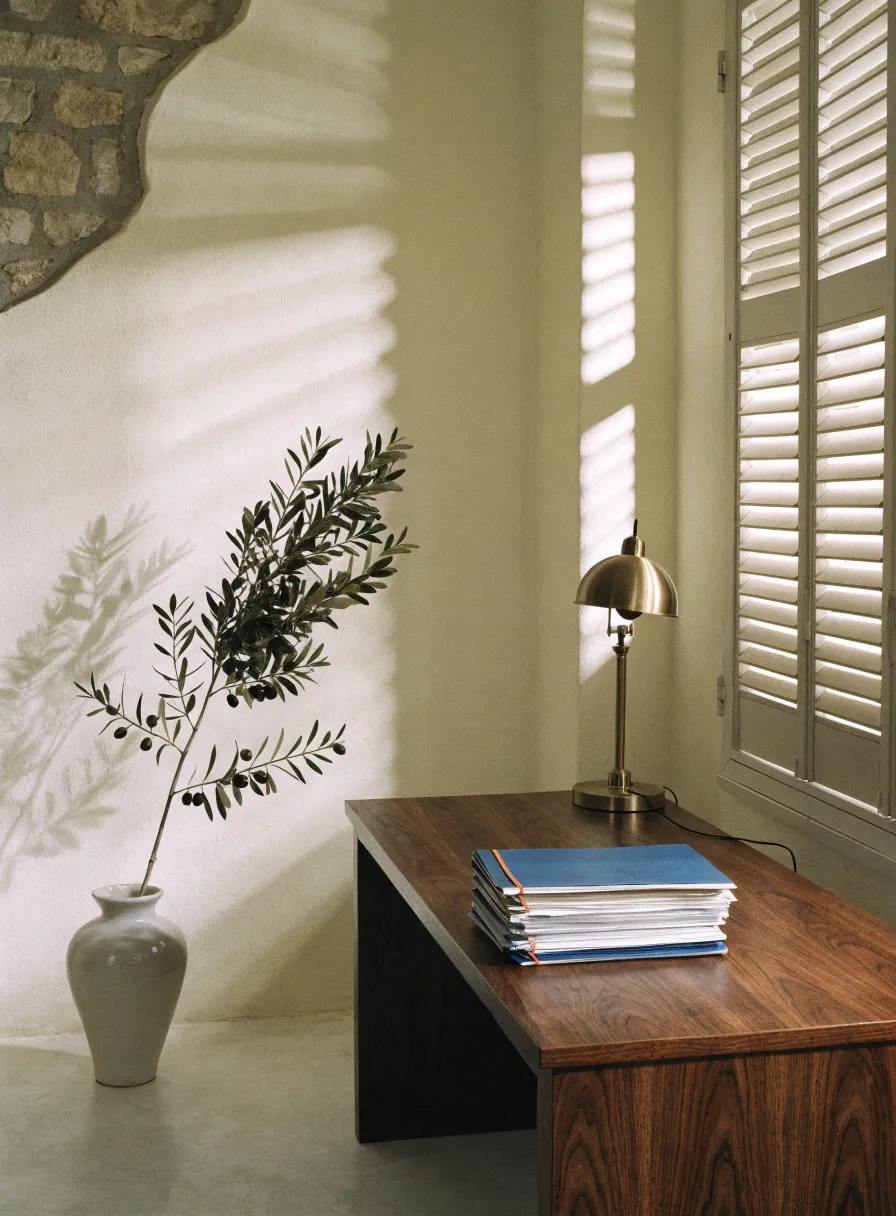 A quiet corner of the agency office: a walnut desk, a brass lamp and a shuttered window